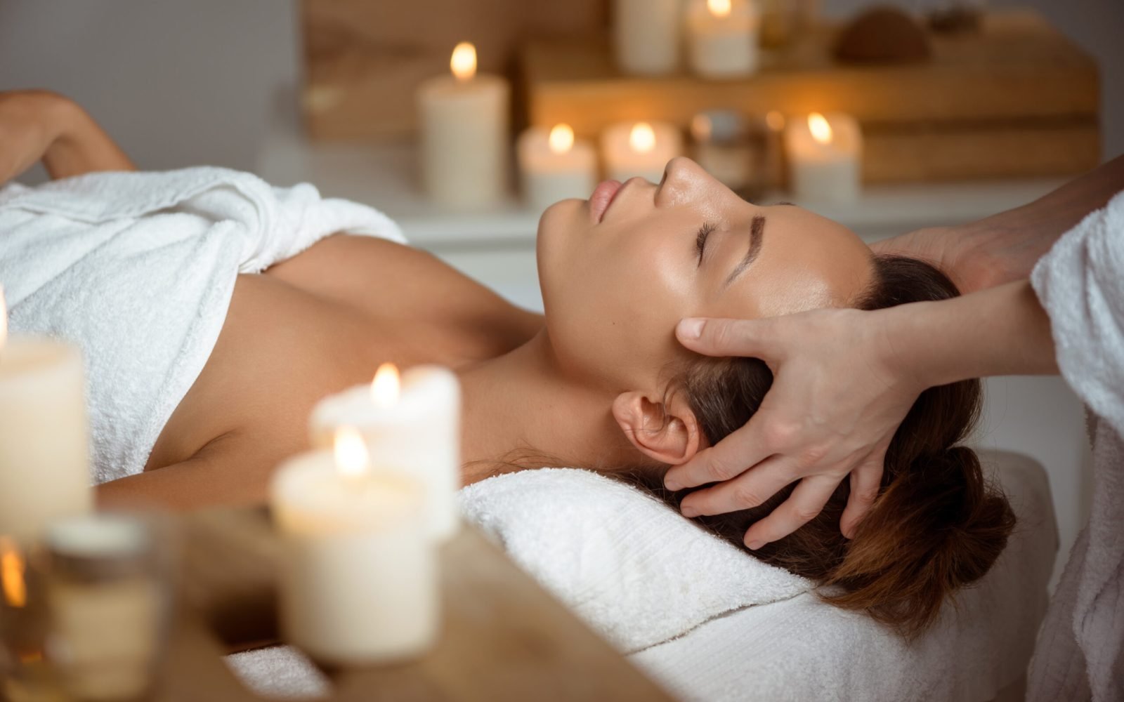 Young beautiful brunette girl having face massage relaxing in spa salon. Eyes closed. Copy space.